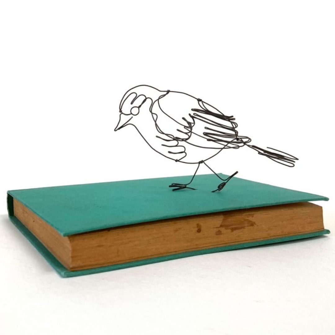 A wire robin, beautifully crafted at the Pod & Pip workshop, perched on top of a book